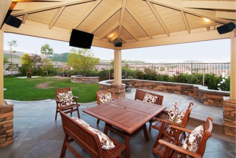 outdoor dining table under a patio with under-eave speakers and a full-shade outdoor TV. 