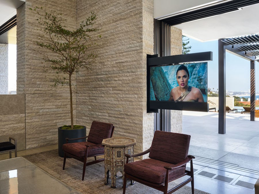 Seating area next to a window with an in-wall TV sliding out of the wall, overlooking the outdoor patio