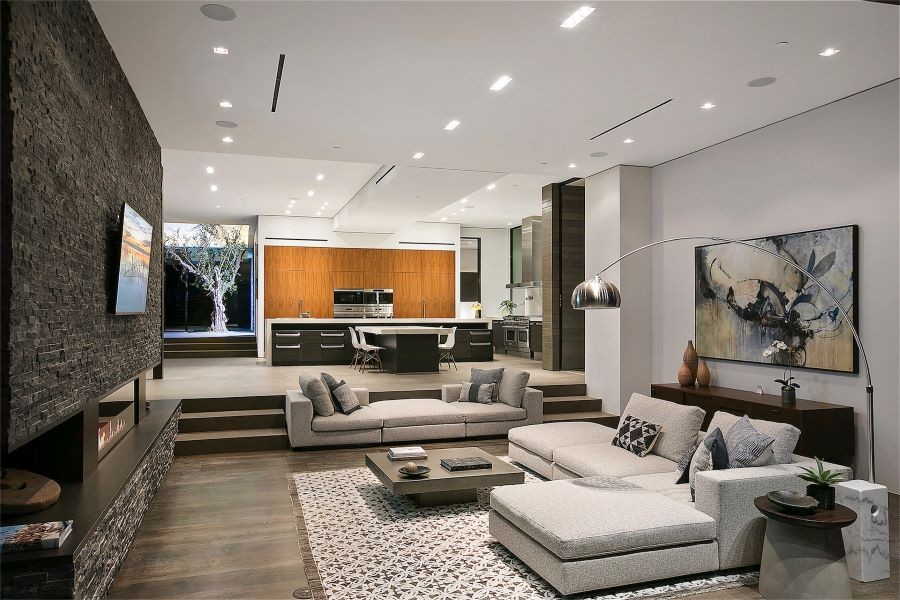 A living room with an open floor plan, in-ceiling speakers, flat-screen TV, and a lit fire feature.