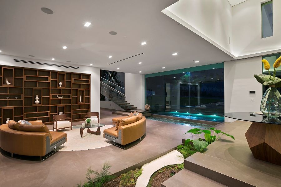 A well-lit living area with plants, natural light, in-ceiling speakers, and a view of the pool.