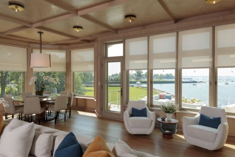A living area with shades half-drawn over windows that look out over the ocean.