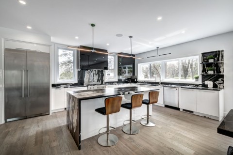 A modern kitchen with a large island and barstools, with in-ceiling speakers.