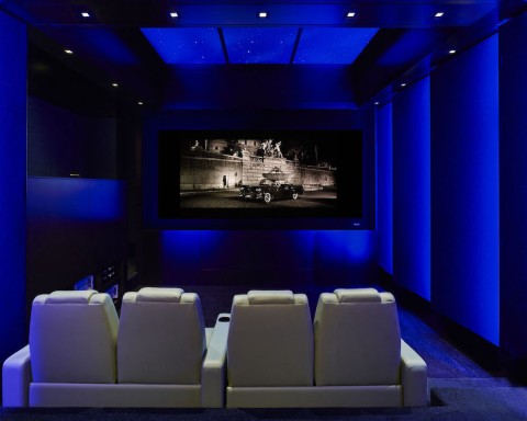 Custom home theater with blue illumination, comfortable seating, and a car display on the screen.