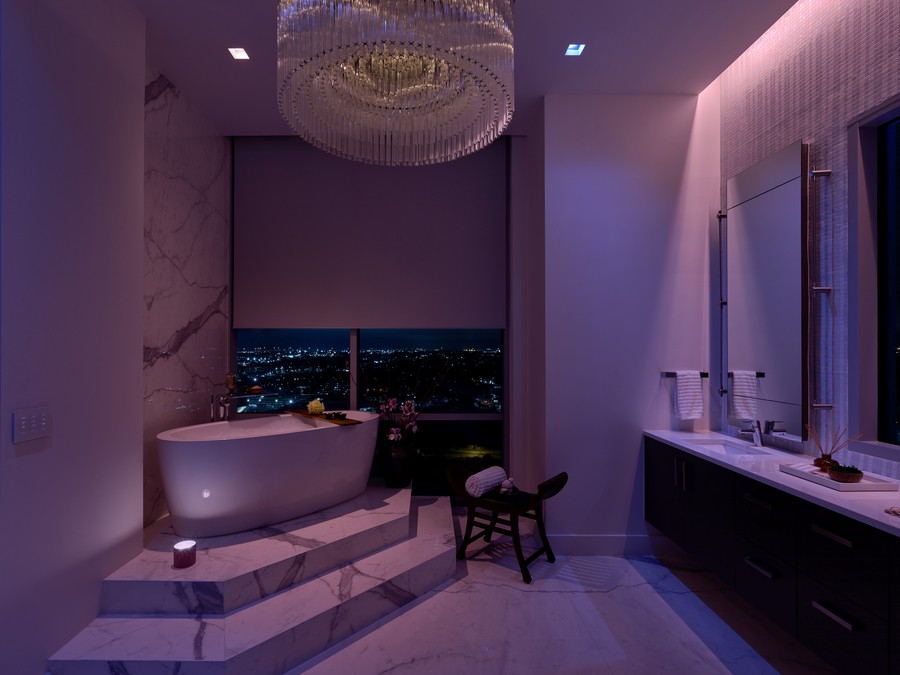 bathtub on top of tiered steps in a luxurious bathroom overlooking the city with purple-pink Lutron lighting