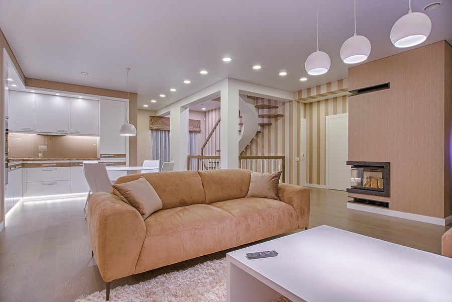 A beautiful, bright living room with a beige couch, hanging light fixtures and recessed lighting in the background.