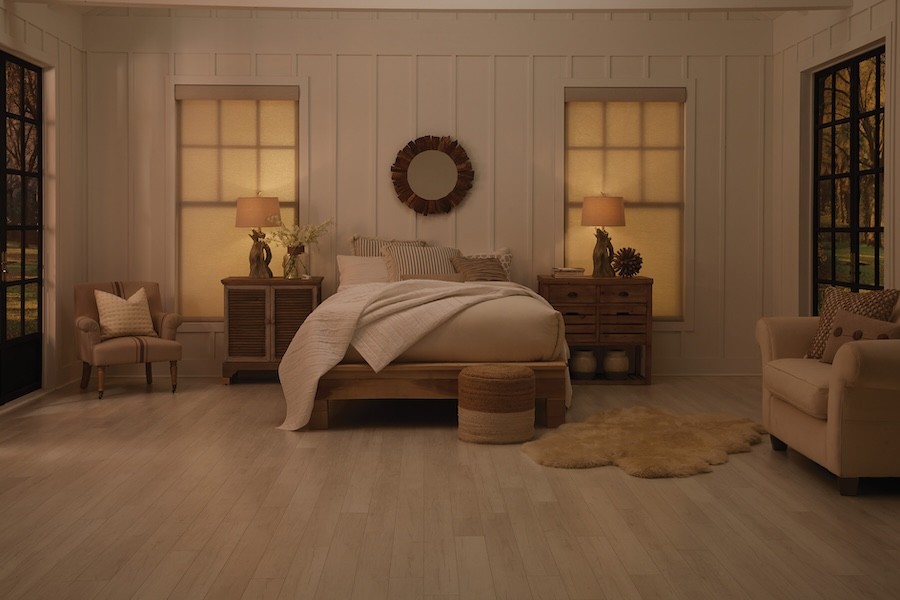 A bedroom with warm, yellow-toned lighting and motorized shades fully drawn.